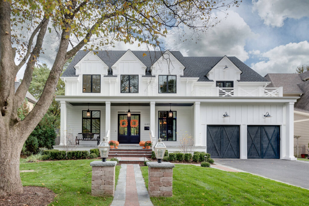 Traditional home exterior with a classic white facade, pitched roof, covered porch, and elegant landscaping. Traditional exterior design by DesignX Studios.